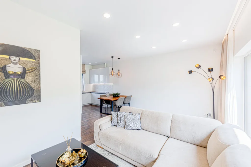 Valgomojo zona su mediniu stalu, moderniu šviestuvu ir šviesiomis sienomis