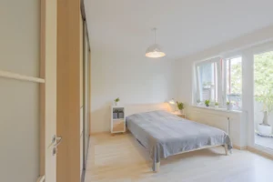 Miegamasis su dvigule lova, šviesiomis grindimis ir spinta su veidrodžiu