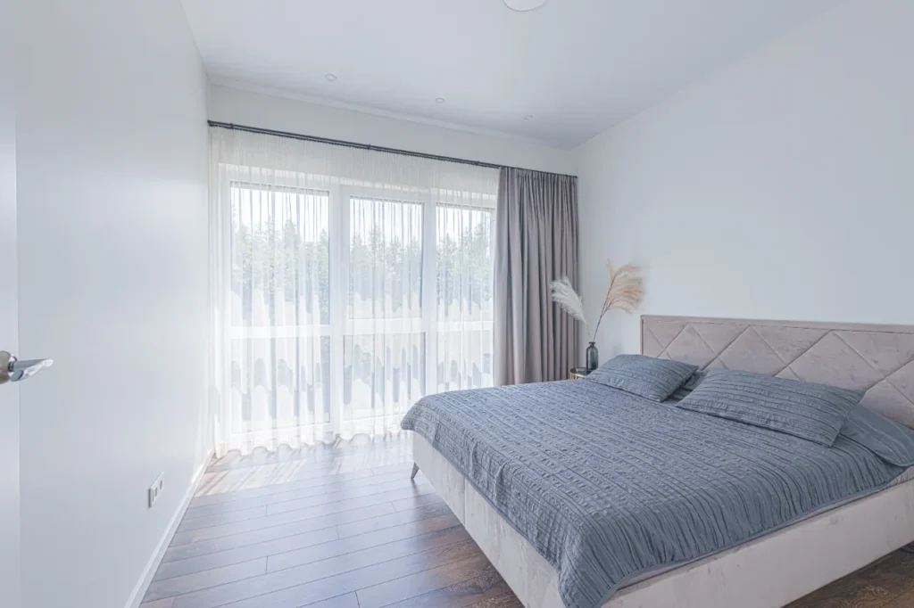 Šiuolaikiškas miegamasis su dideliais langais ir tamsesniu parketu