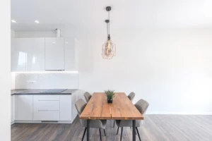 Pilka svetainės sofa su valgomojo stalu ir televizoriumi šviesioje patalpoje